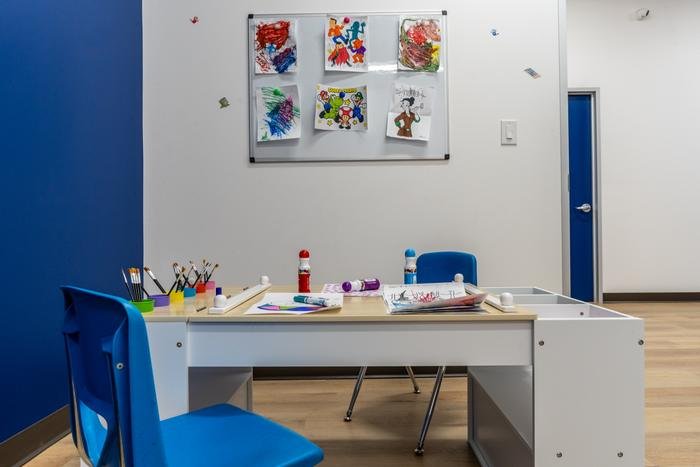 An art table set with brushes and paint, below a board of children's drawings and paintings.