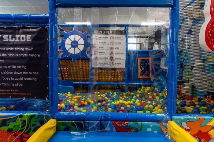 The ball pit inside the indoor playground, with a ship's wheel, a slide and the rules of play posted where children can see them.