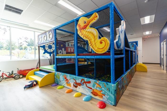 The indoor playground at SOS McKinney, a two-level soft-play structure with netting, a slide and a large seahorse panel beside a window.